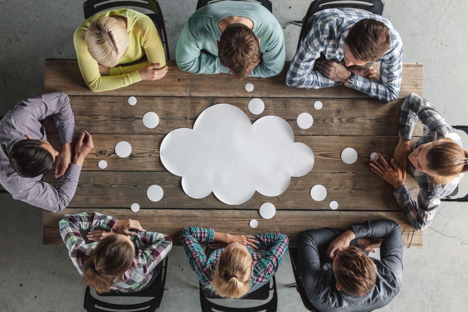 Group of people sitting around a table covered with paper speech bubbles banner image