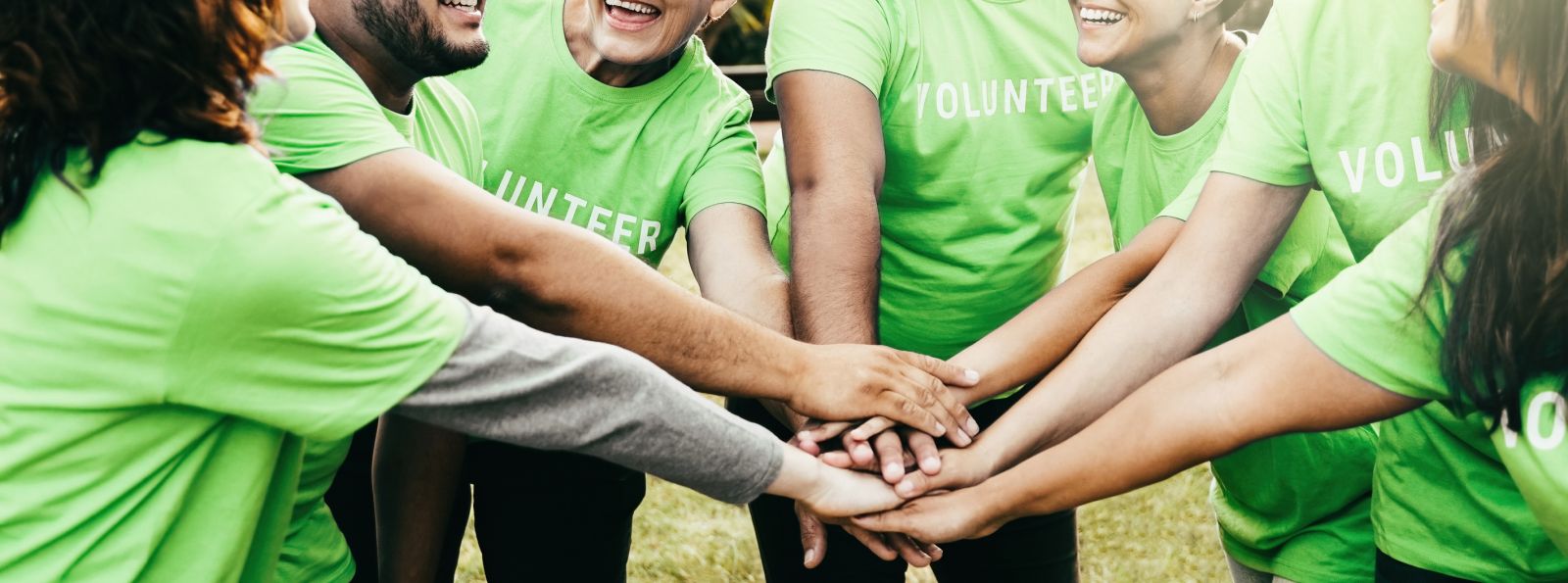 Group of people wearing green volunteer t-shirts putting their hands together in the middle of a circle banner image