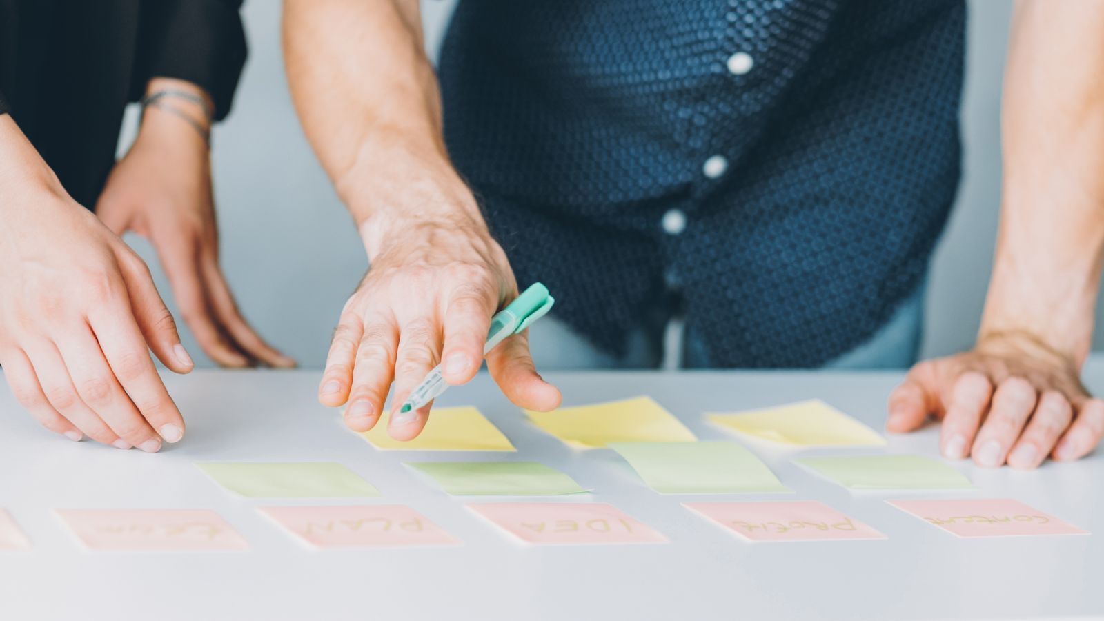 Coloured post it notes on a desk with a figure behind the desk holding a pen banner image